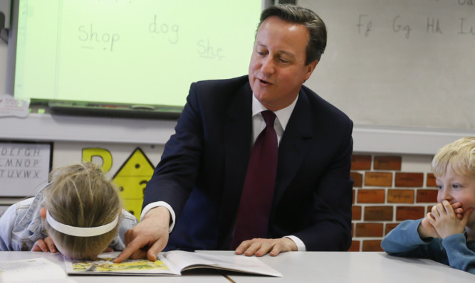 David Cameron reads a book to Lucy Howarth, 6, and Joshua Davies, 5, during a visit to Sacred Heart RC primary school in Westhoughton near Bolton.