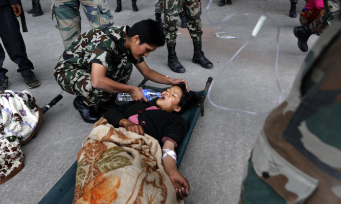 An Indian Army doctor helps an injured woman drink water after she was evacuated from higher reaches of mountains by Nepalese army.