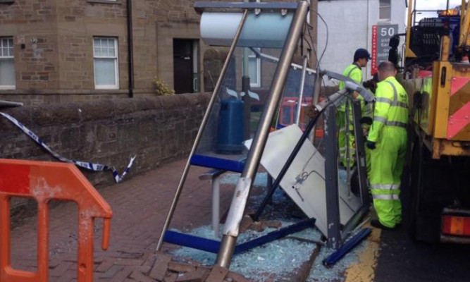 Workmen inspect the smashed bus shelter.