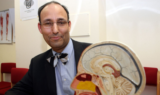 Photo shows Sam Eljamel next to a model of a human skull and brain.