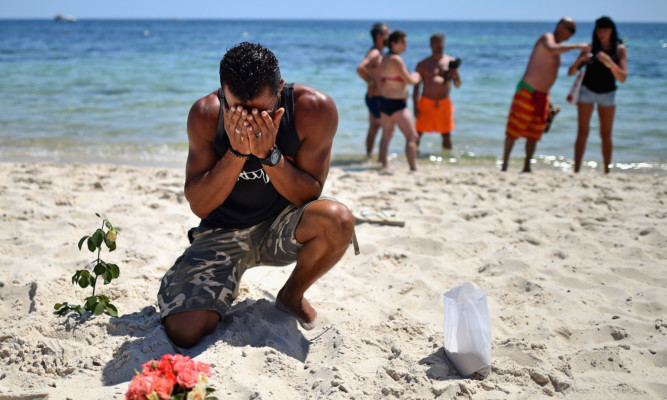 A man prays after laying flowers on Marhaba beach where 38 people were killed.