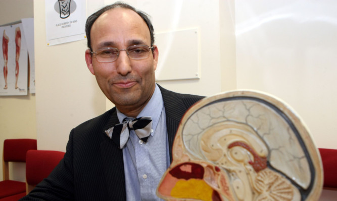Surgeon Sam Eljamel at Ninewells Hospital in Dundee, smiling next to a model of a human head opened to show the brain.
