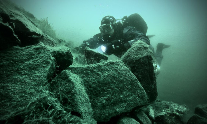 A diver examines rocks in murky waters at the bottom of Prestonhill Quarry.