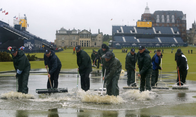 Course officials clear standing water as rain suspends play at The Open.