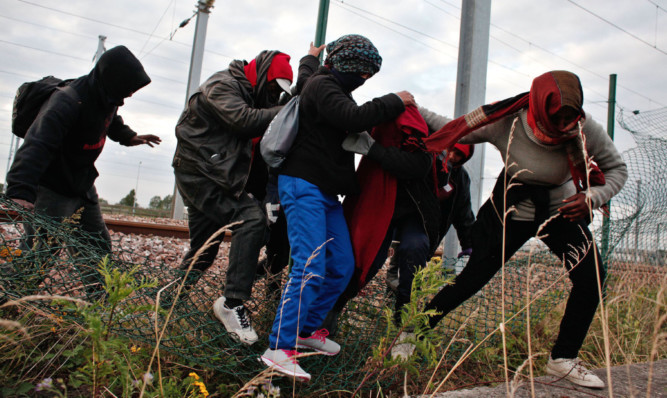 Migrants step over a fence as they escape from railway police officers, in Calais, northern France. David Cameron has come under fire for describing the migrants as a "swarm".