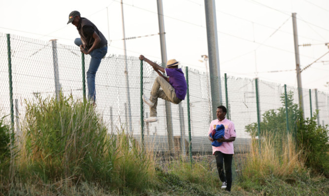 Migrants climb over a fence on to the tracks near the Eurotunnel site at Coquelles in Calais.