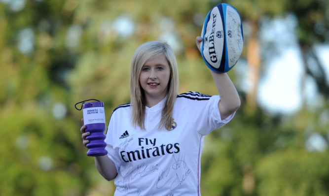 Kirsten Cameron wearing the signed Real Madrid top and holding a rugby ball signed by the Scotland team.