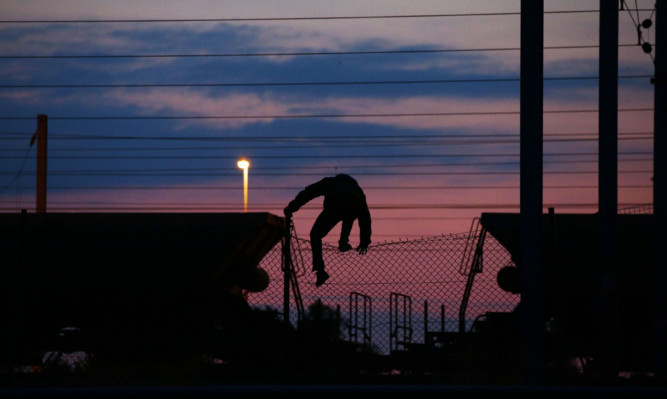 A migrant climbs over a fence on to the tracks near the Eurotunnel site at Coquelles in Calais.