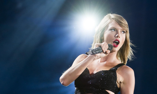 photo shows singer Taylor Swift singing into a microphone under a spotlight.