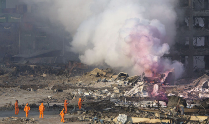 Fire fighters in protective gear watch as smoke continues to billow out after an explosion at a warehouse in northeastern China's Tianjin municipality.