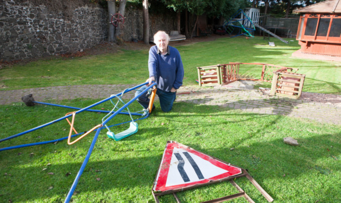 Robert Stark with the vandalised play equipment and a road sign that was flung into his garden.