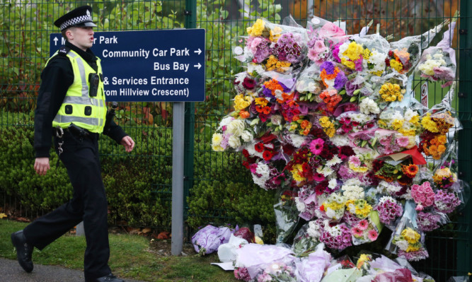 A police officer passes by the growing floral tribute to Bailey Gwynne outside Cults Academy.