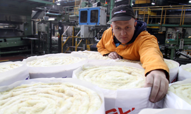 A worker inspects rolls of Superglass insulation.