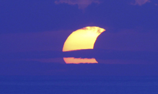 The partial eclipse seen through cloud at Sanur beach, Bali.