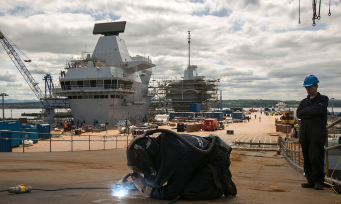 A construction worker welds metal on the flight deck of HMS Queen Elizabeth aircraft carrier in Rosyth. The contract for its accompanying tug boat has been given to a Dutch company.