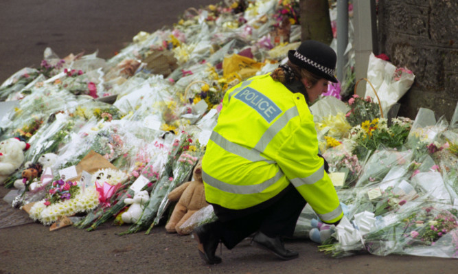Woman police officer laying a bouquet on top of a large mound of flowers outside Dunbland Primary School following the 1996 shooting.
