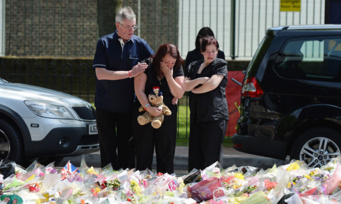 Holding a teddy bear Lyn Rigby, mother of Drummer Lee Rigby, with other family members look at some of the thousands of floral tributes left outside Woolwich Barracks.