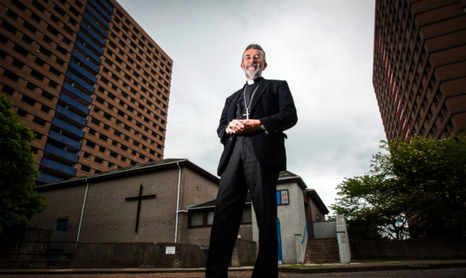 Rev Peyton in front of the church, which is dwarfed by the multi-storeys.