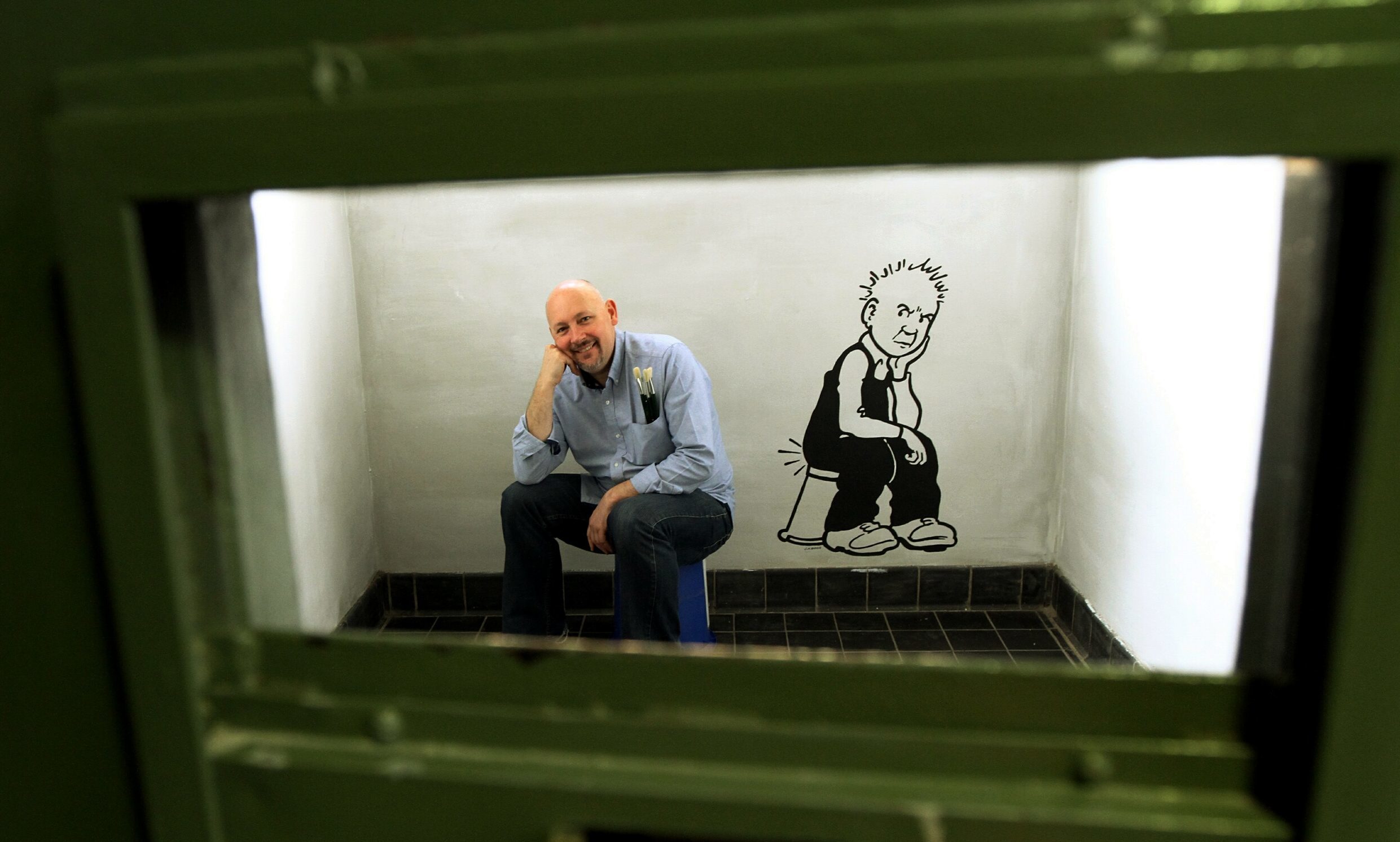 Artist John Barrie in one of the cells beside his artwork of Oor Wullie.