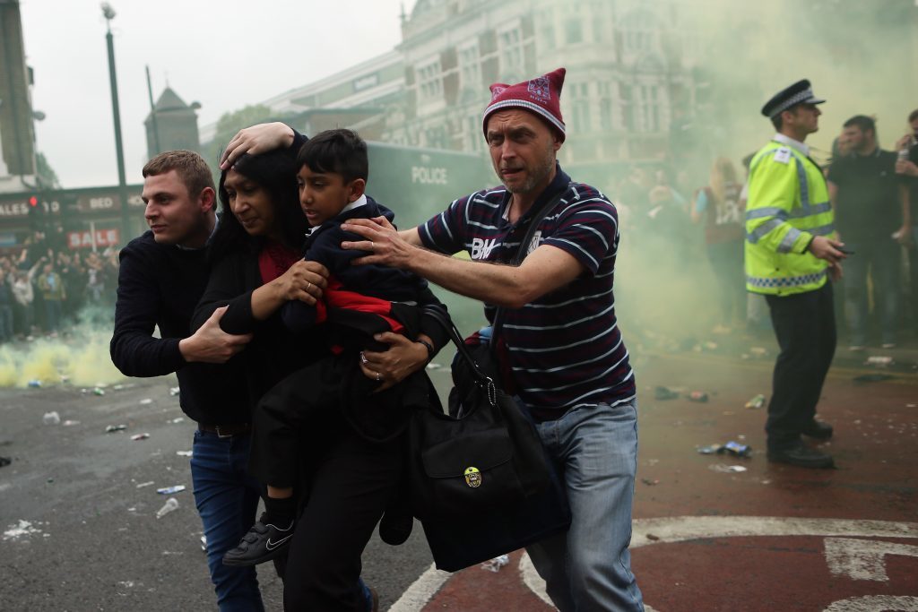 LONDON, ENGLAND - MAY 10: A woman and a child are helped past West Ham fans as people become violent and start throwing bottles at police outside the Boleyn Ground on May 10, 2016 in London, England. Tonights Premier League match against Manchester United is West Ham United's last game at the Boleyn Ground, bringing to an end 112 years of the club's history at the ground. The club will move into the Olympic Stadium next season, making way for developers and plans for 800 new homes where the stadium now stands. (Photo by Dan Kitwood/Getty Images)