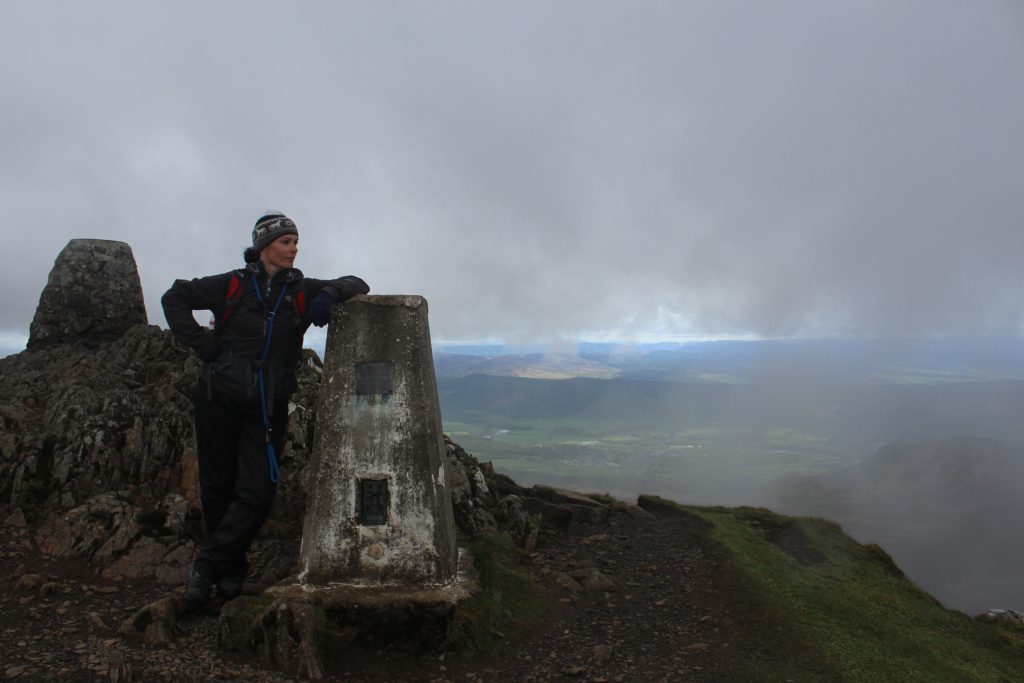 Gayle enjoys the misty view from the trig pillar on Ben Vrackie. 