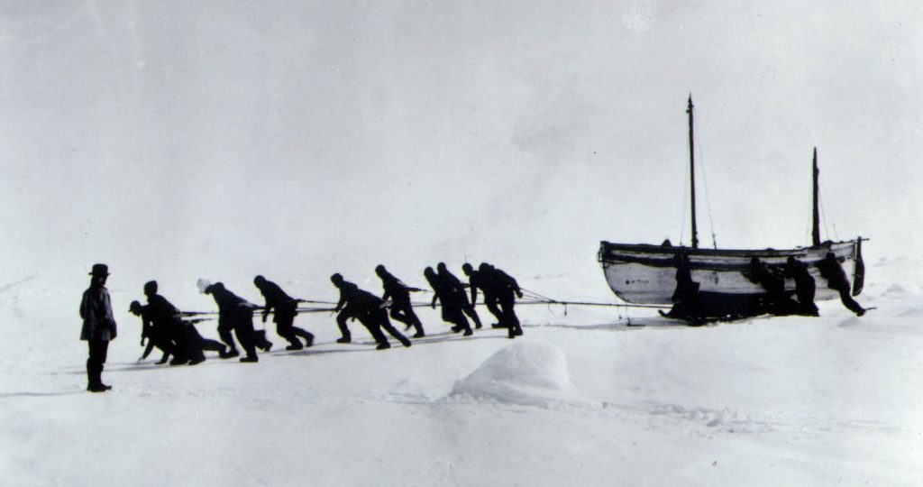 The crew hauling the James Caird across the Antarctic wastes after their ship the Endurance broke up, with Shackleton looking on.
