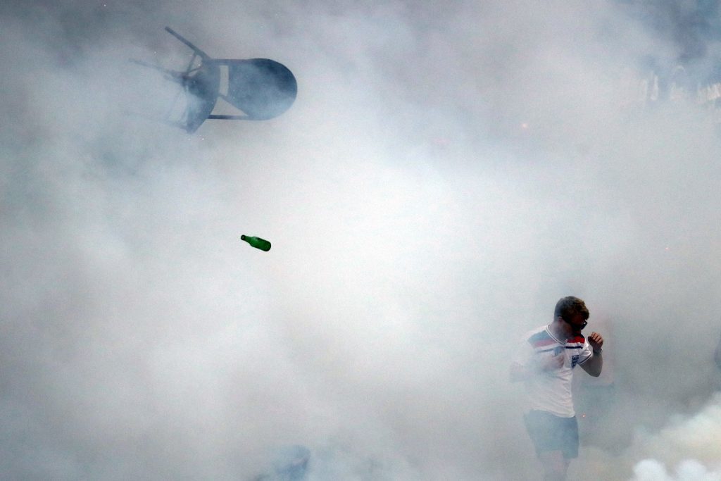 A bottle and chair are thrown as an England fan walks through tear gas.