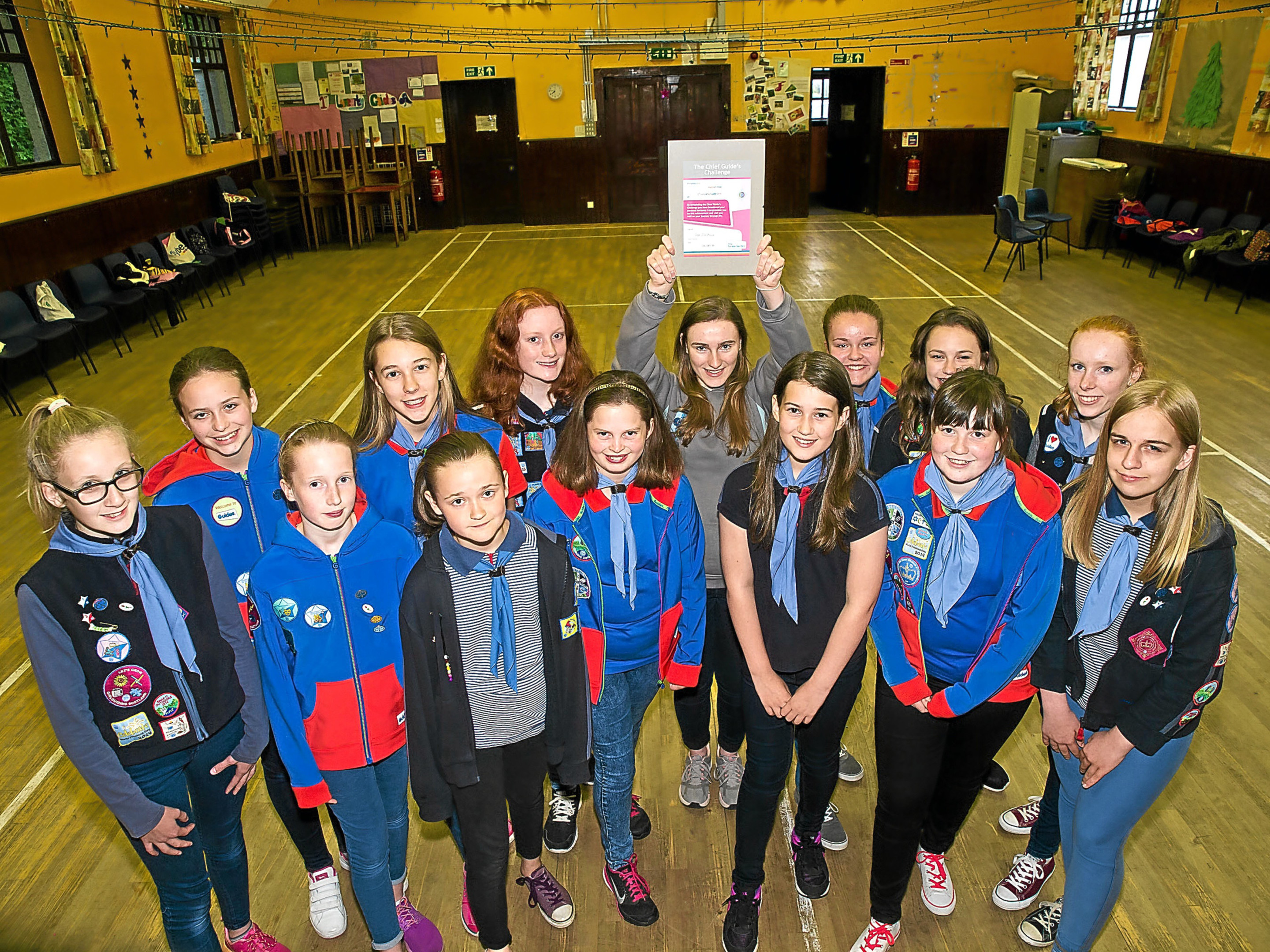 Hannah Haig holds aloft the Chief Guide's Challenge Award for young leaders surrounded by other guides in Luncarty village hall.