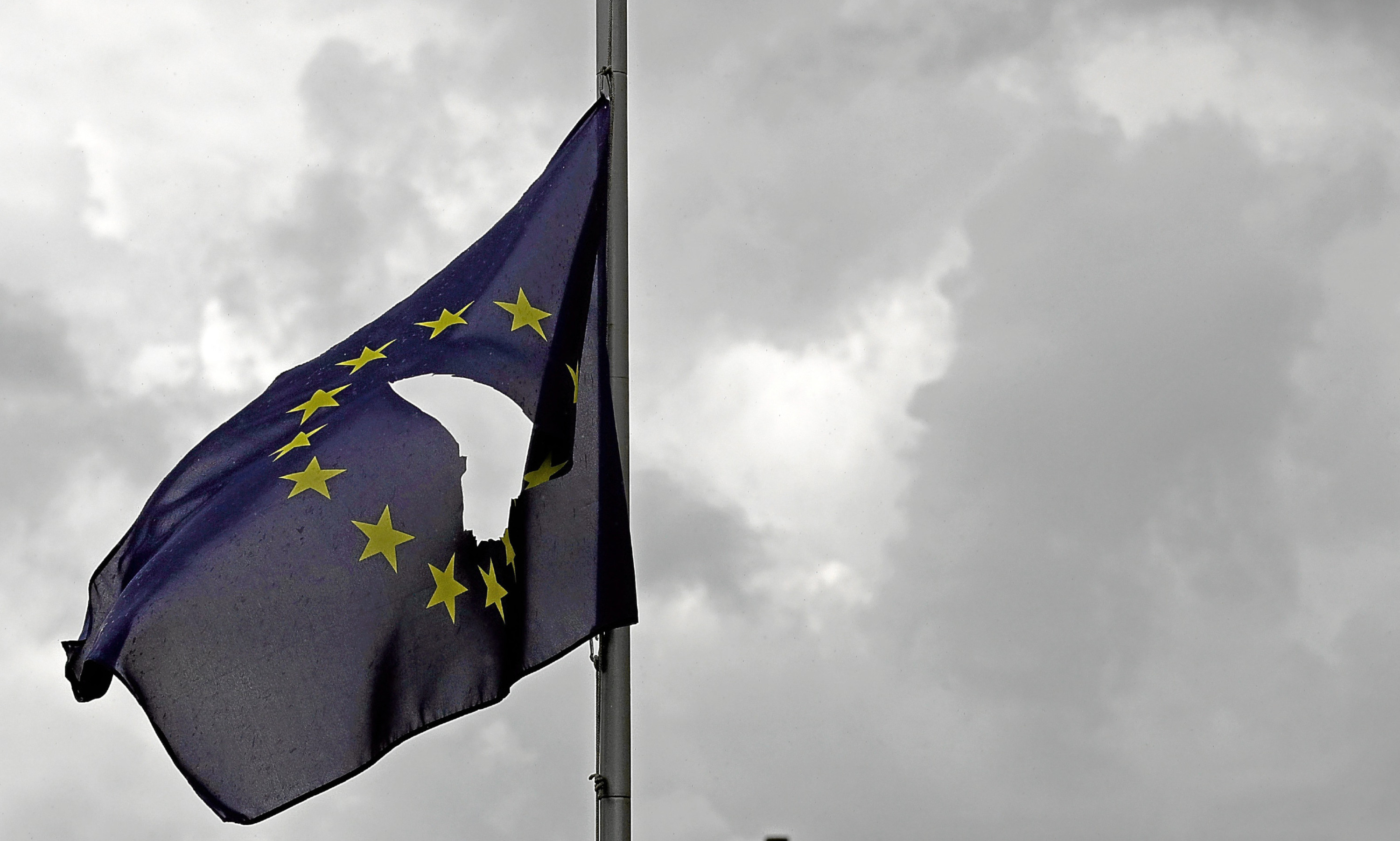 A European Union flag, with a hole cut in the middle, flies at half mast.