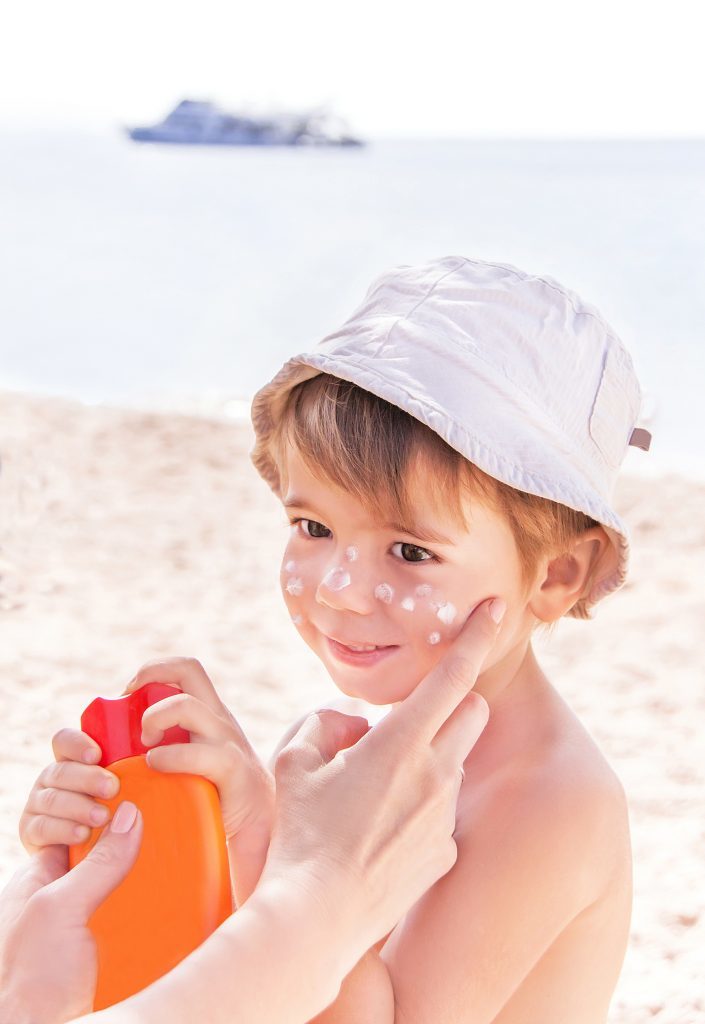 Hand of mother applying suncream to her son on beach.