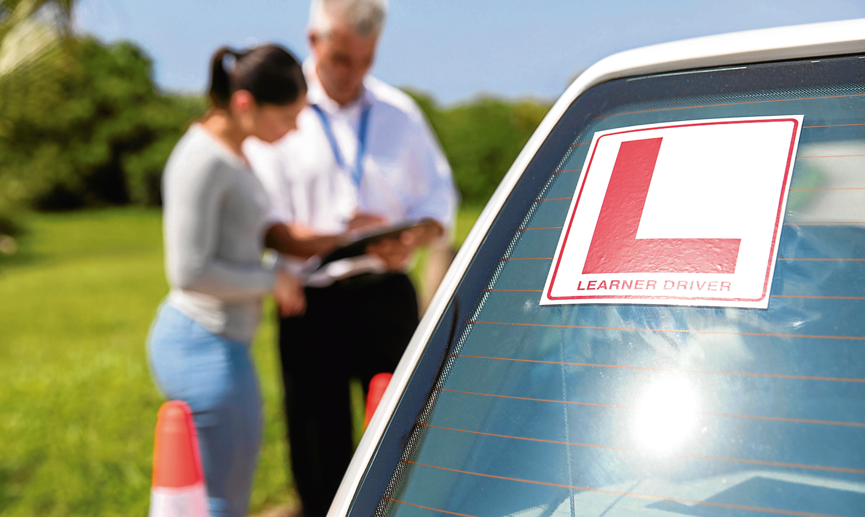 learner driver sign on a car with student and instructor standing behind