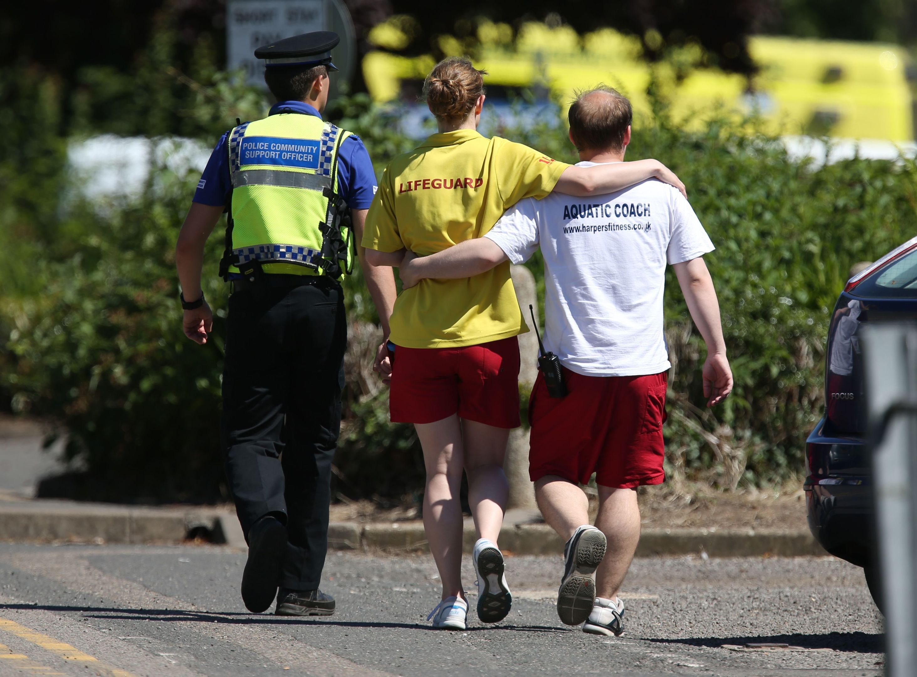 A lifeguard and swimming coach are escorted by a community support officer as they walk towards Castle Swimming Pool in Spalding, Lincolnshire, after three people including a suspected gunman have been shot dead.