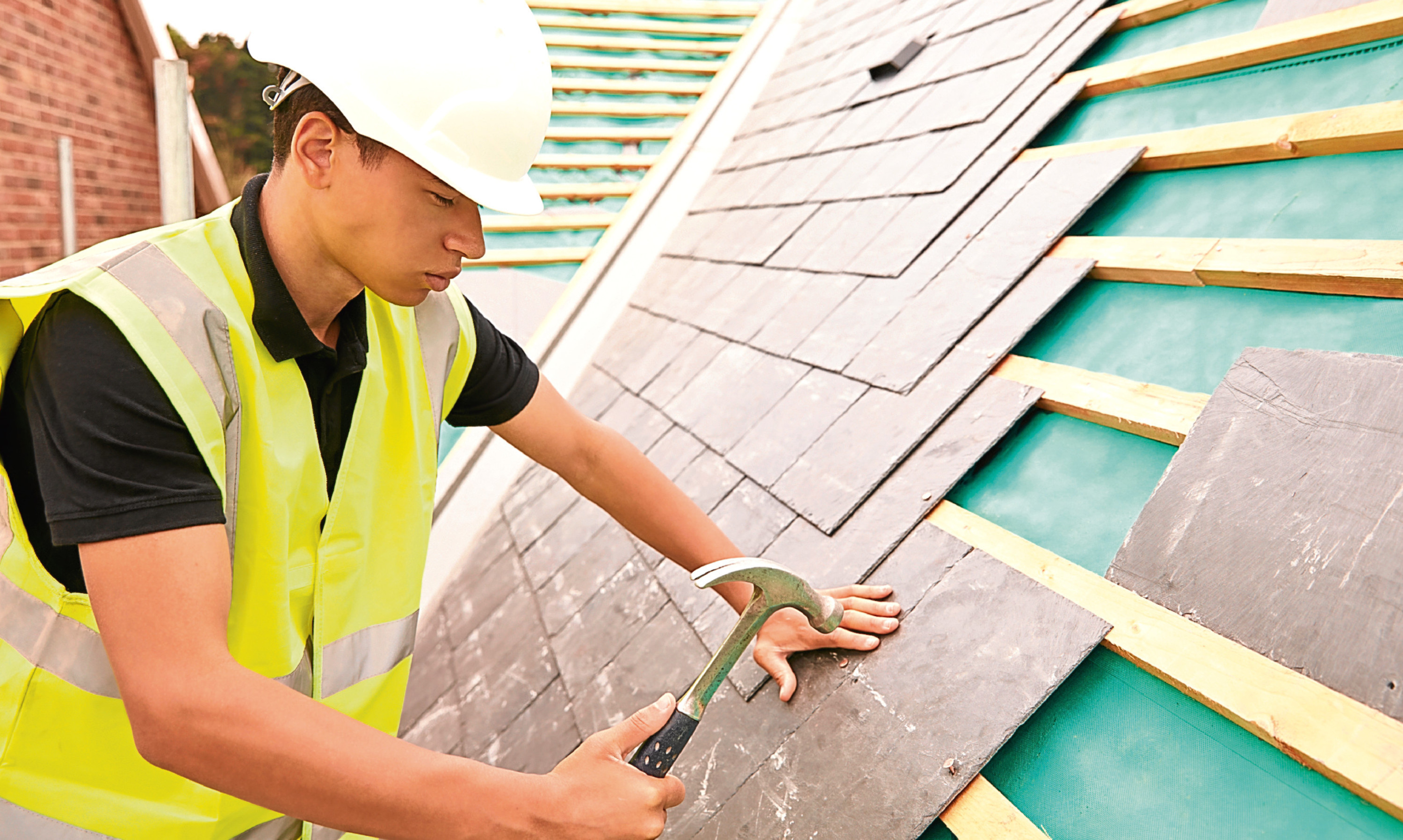 A construction worker lays slate roof tiles