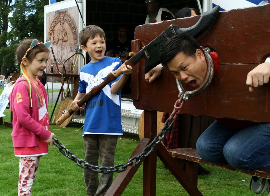 Rebecca, 4, and Aiden Lum, 7, with dad Chris in the stocks.