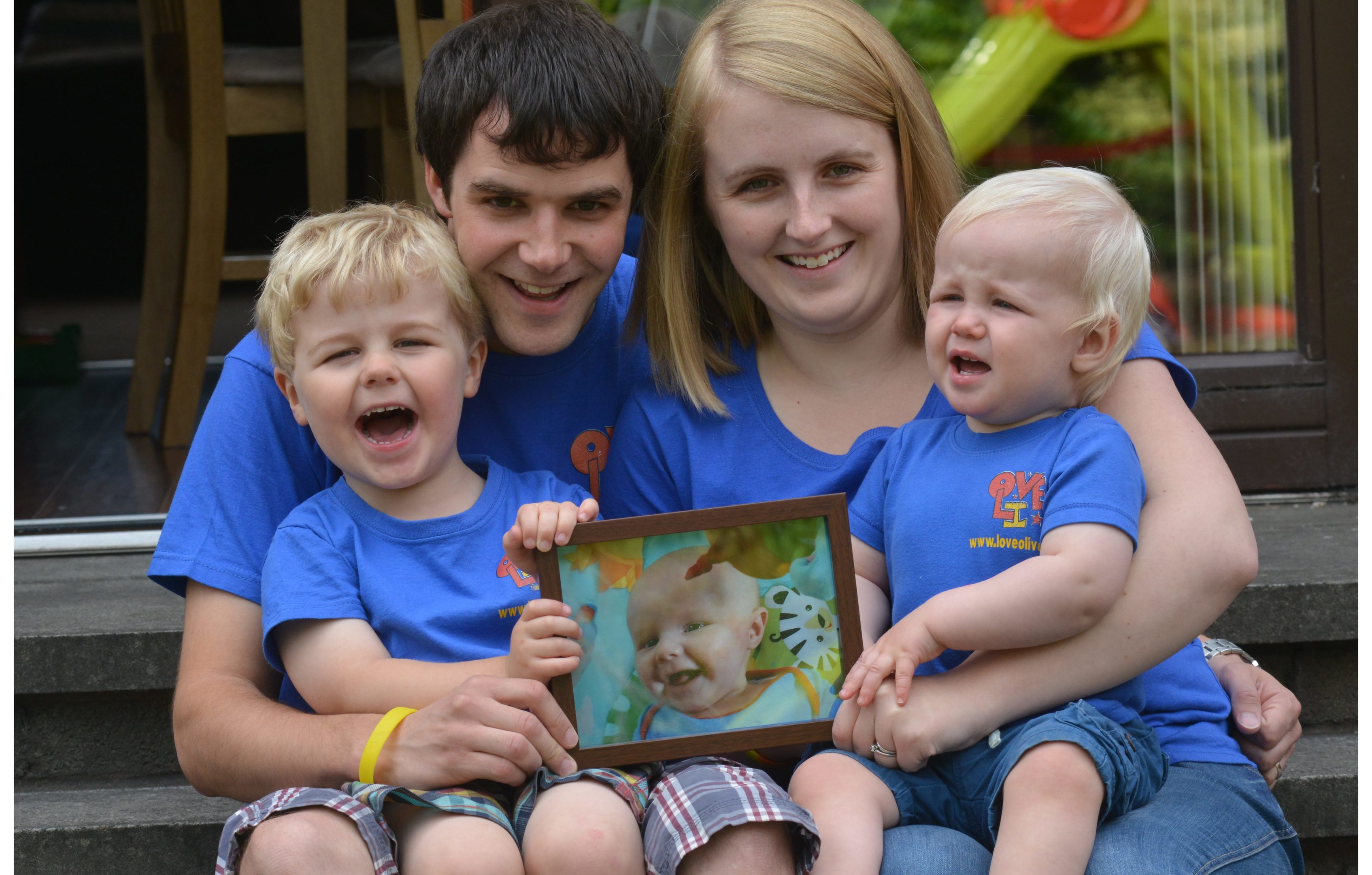 Andy and Jennifer Gill with Micah and Rory  holding a pic of son Oliver.