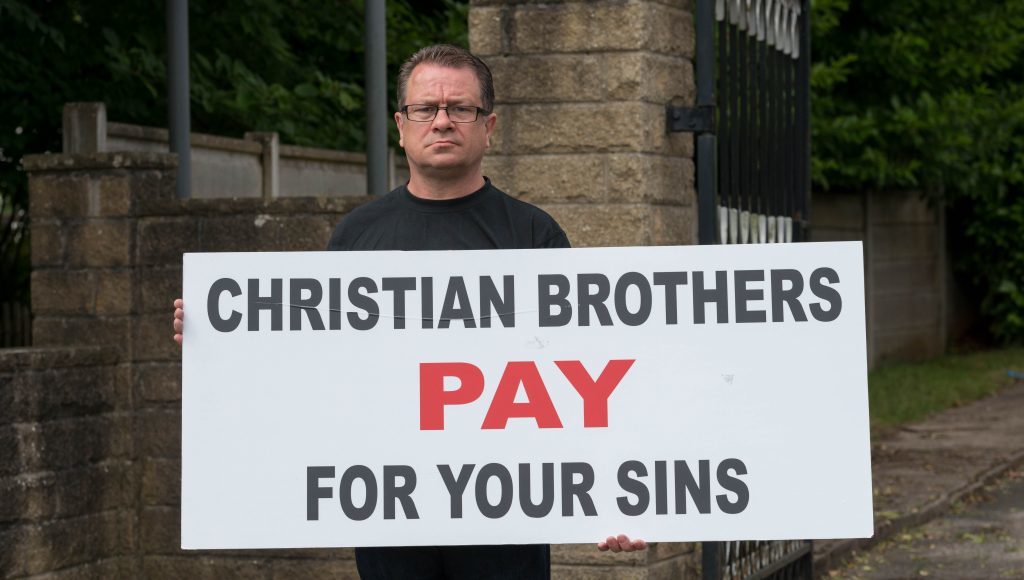Dave Sharp protesting with a banner outside the Christian Brothers premises of Woodeaves, Wicker Lane, Hale Barns, Altrincham, Cheshire, on Thursday June 23 2016
