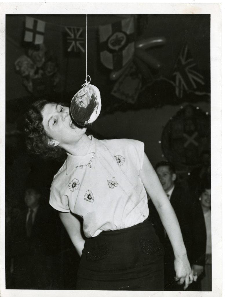 A young Dundee woman attempting to eat a treacle scone hanging from a string. November 1957.