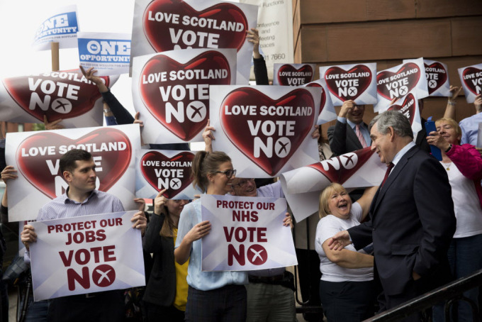 Two Yes campaign posters are held up at top left, beside a group of No campaign supporters holding up posters as former British Prime Minister and No campaigner for the Scottish independence referendum Gordon Brown, right, briefly speaks to them as he leaves after delivering a speech at a No campaign event in Glasgow on September 17, 2014