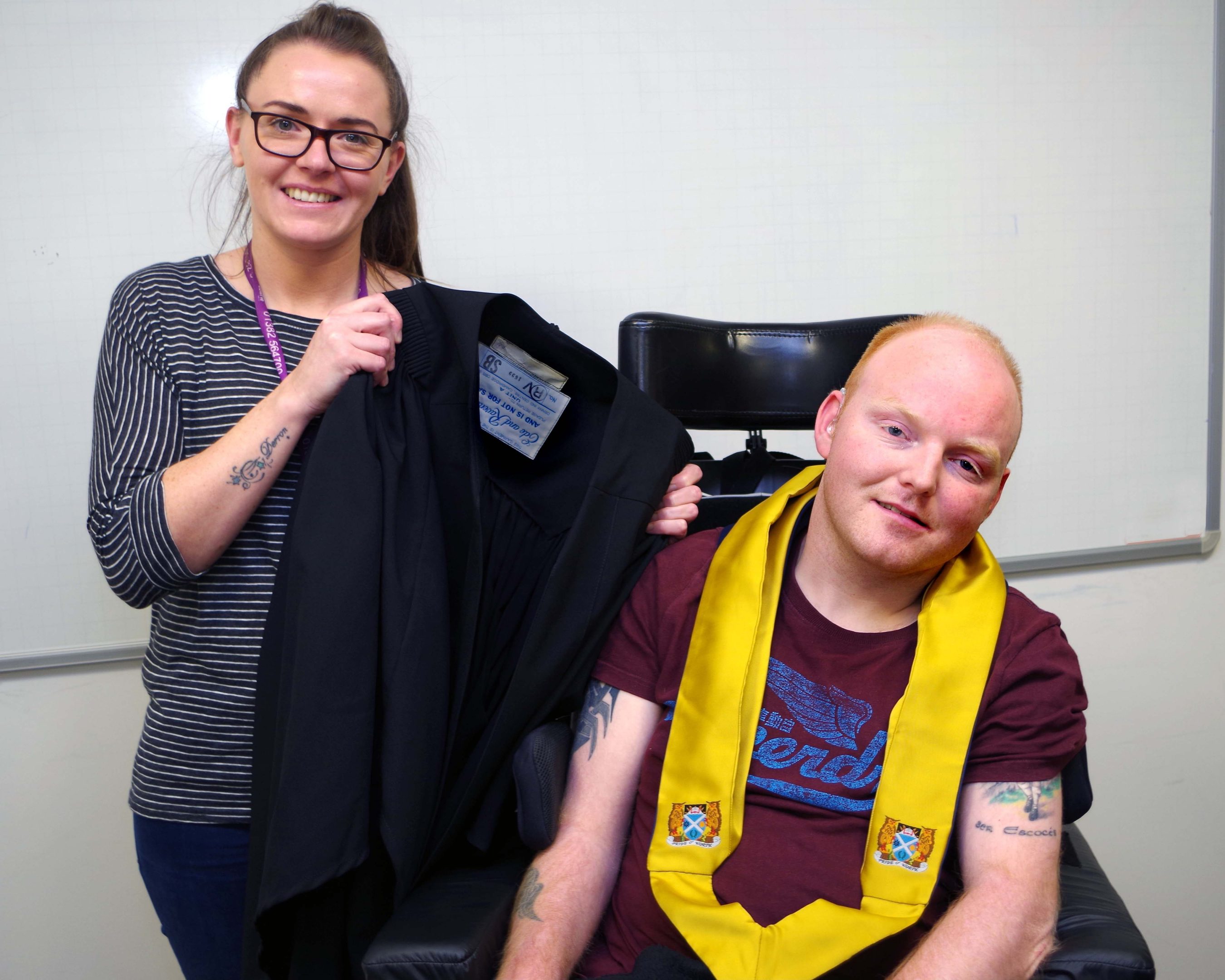 Stewart tries on a graduation robe with the help of Alanna Duncan, support worker for Gowrie Student Support.