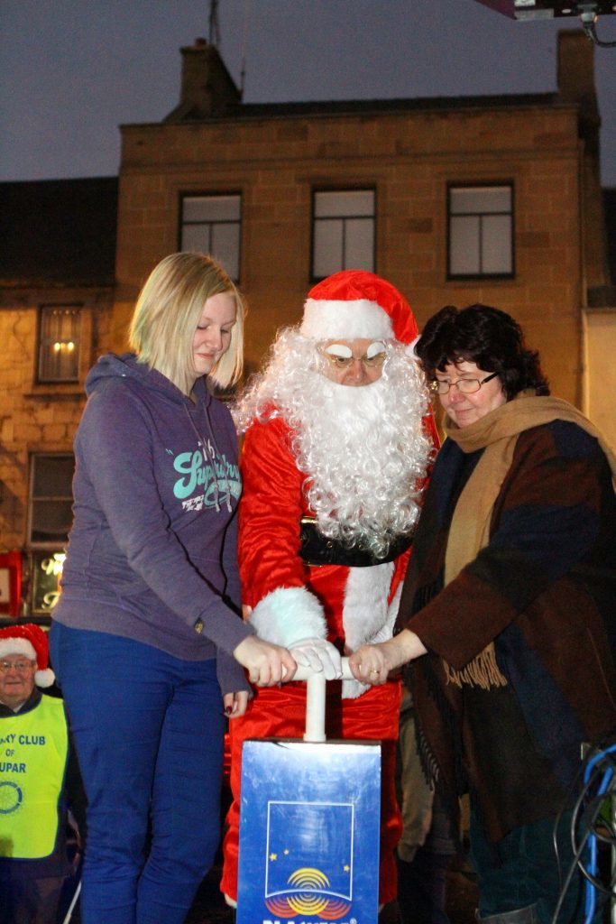 Santa is helped to switch on the Cupar Christmas lights by Young Citizen Of The Year Alana Isbister, left, and Citizen Of The Year Sue Jack
