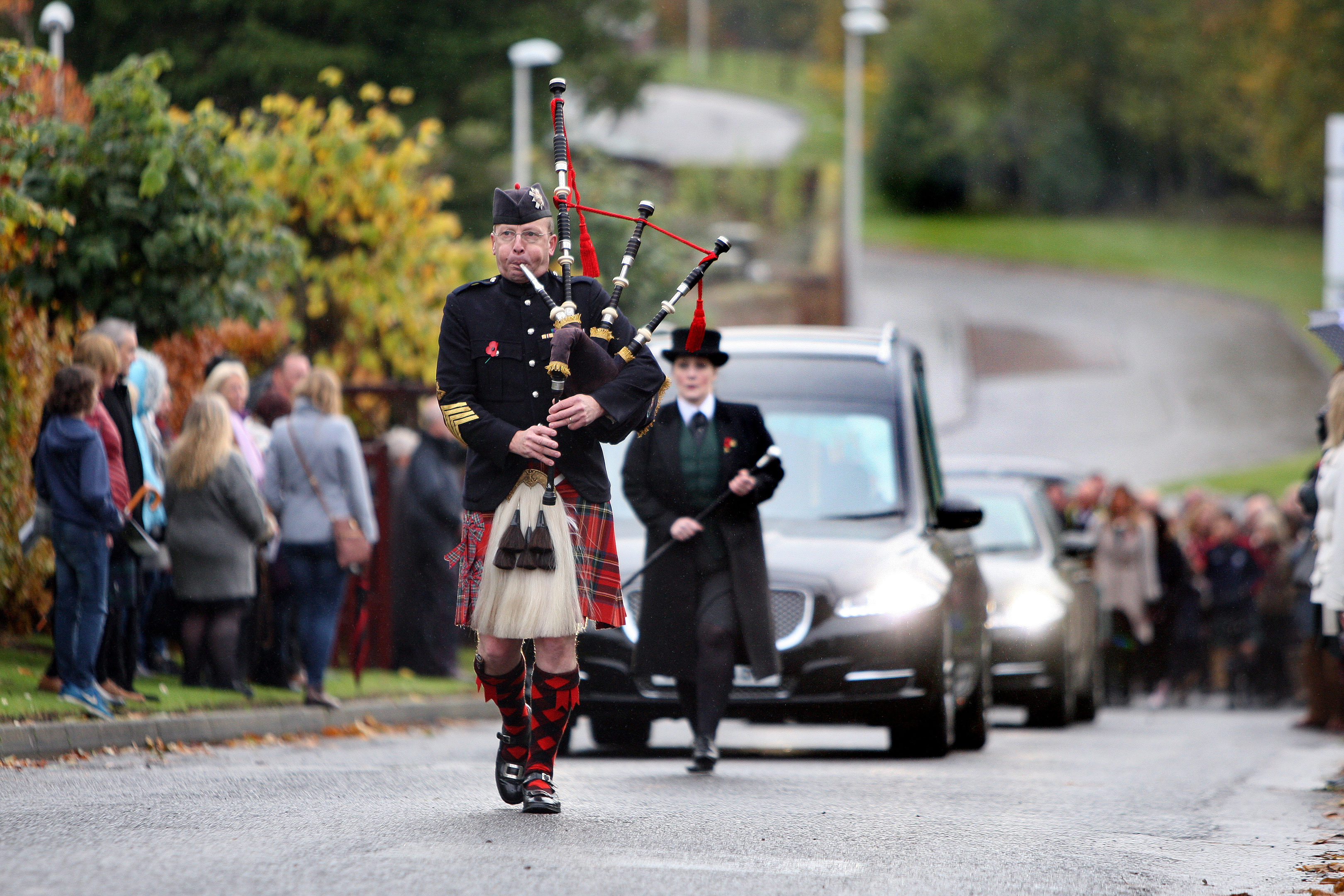 A piper leads the hearse carrying Ewen Chisholm and followed by hundreds of mourners on way to Kirriemuir cemetery,