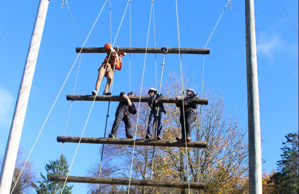 Gayle climbs up the suspended ladder, flanked by scout leaders.