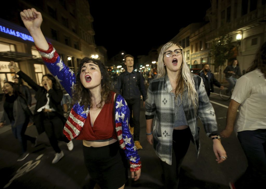 Madeline Lopes, left, and Cassidy Irwin, both of Oakland, march with other protesters in downtown Oakland, California