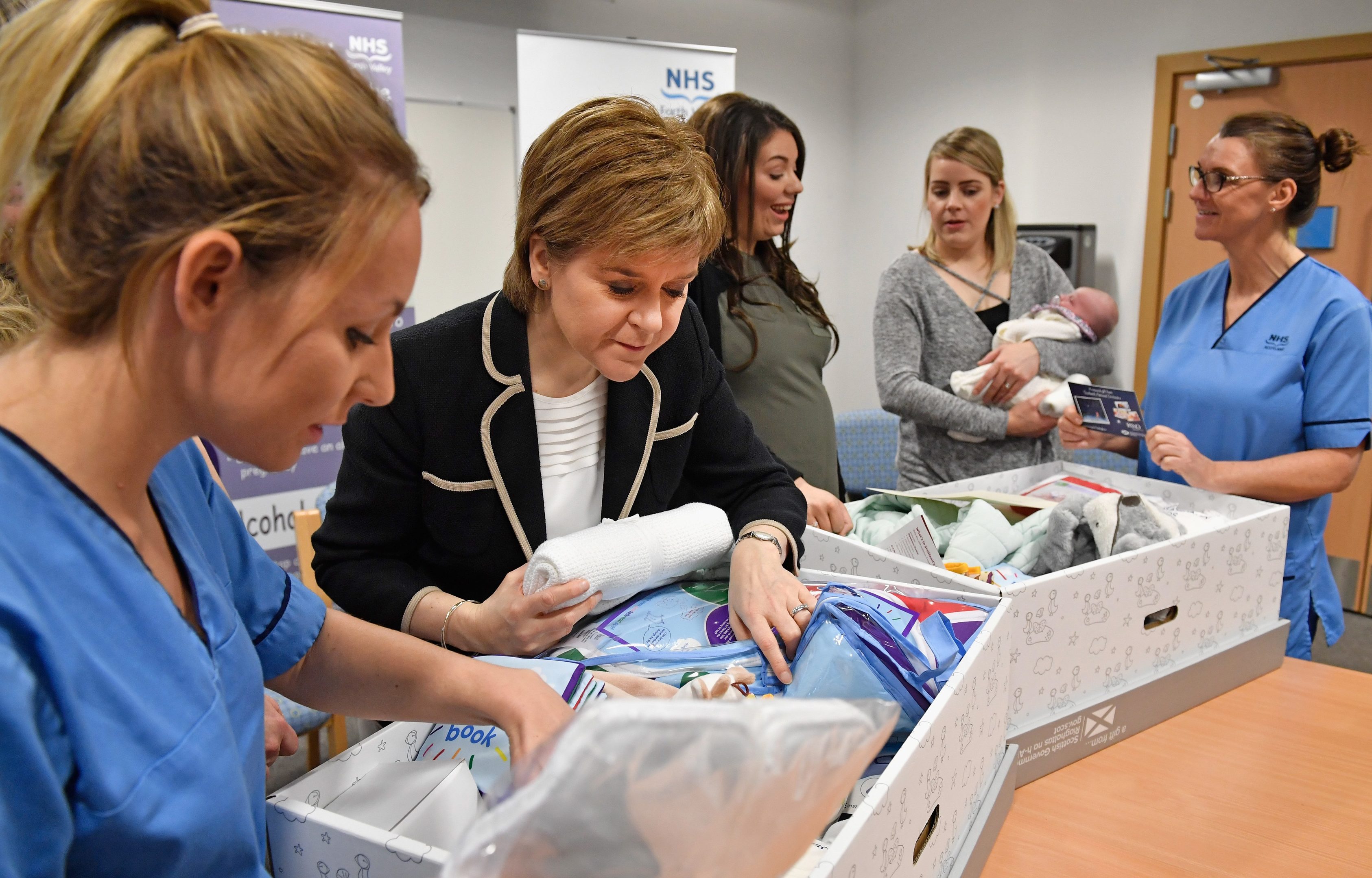 First Minister of Scotland Nicola Sturgeon meets with midwife Rachel Boyland, Toni Akande, Gail and Libby Mellor and midwife Sheila Lannon as she gives out Scotland's first baby boxes at Clackmannanshire Community Health Centre