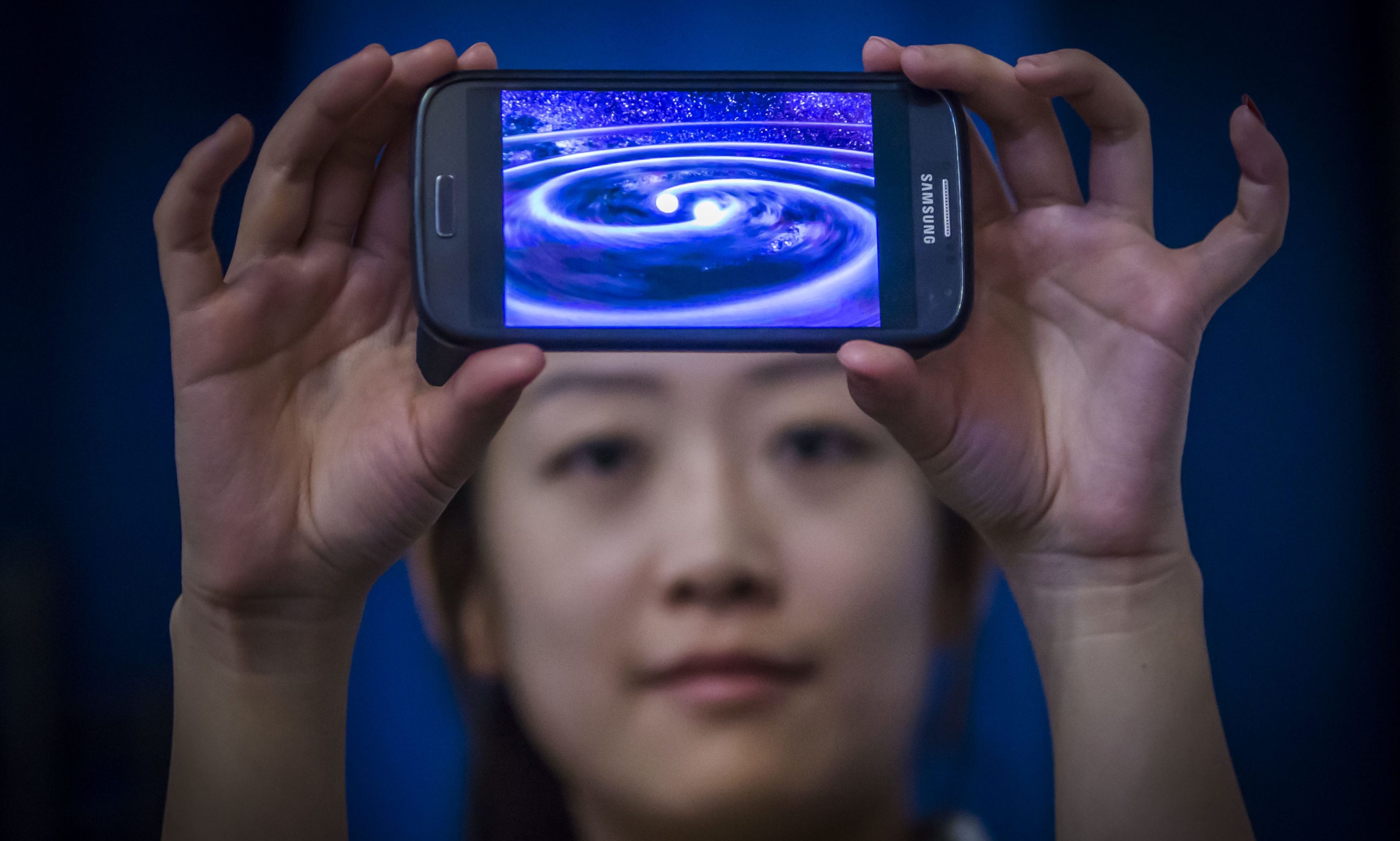 Student Muzi Li at the Institute of Gravitational Research at Glasgow University holding a phone that shows a computer simulation of gravity waves - ripples in spacetime - which have been detected by scientists a century after Albert Einstein predicted their existence.