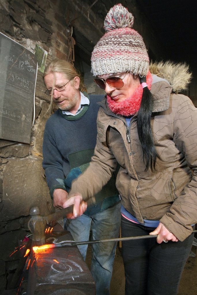 Jim guides Gayle through some basic blacksmithing skills.