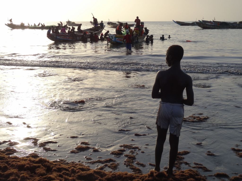 A young boy watches the fishing boats as the sun sets in Tanji. 