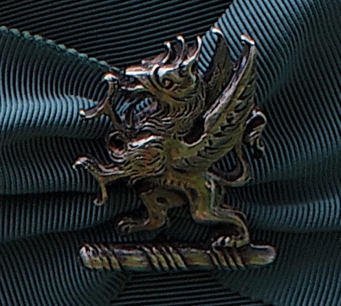 The cap badge, representing the family's ‘Dancing Beastie’ crest.