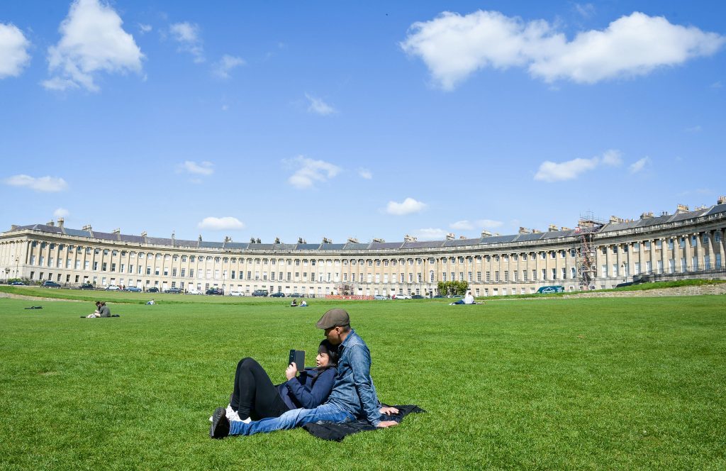 People relax in the sunshine on the lawn in front of the Victorian Royal Crescent, Bath.