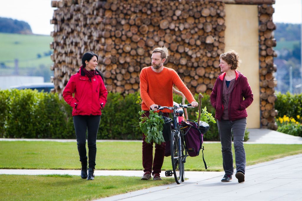 Gayle and Sarah flank Jonathan, who pushes his bike carrying raspberry bushes ready to be planted.